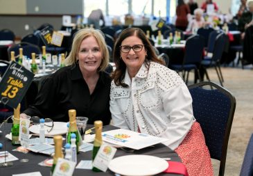 Two women pose at Chamber Bingo Night with bingo cards and champagne on the table